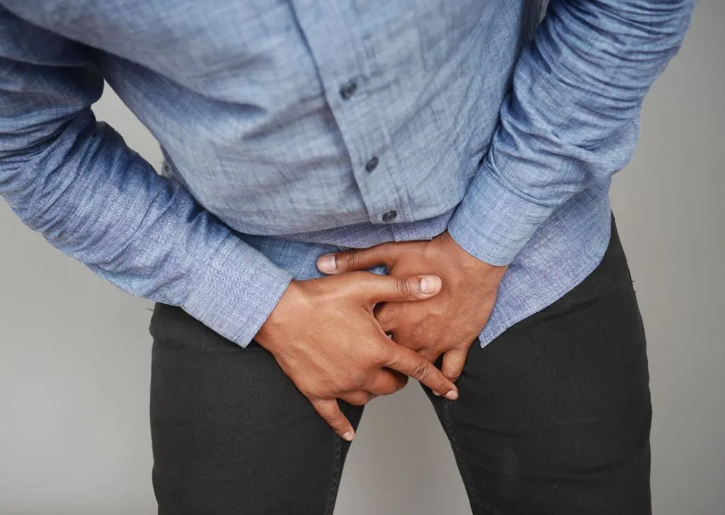 A man applying pressure on his groin due to pain caused by frenulum breve tear. 