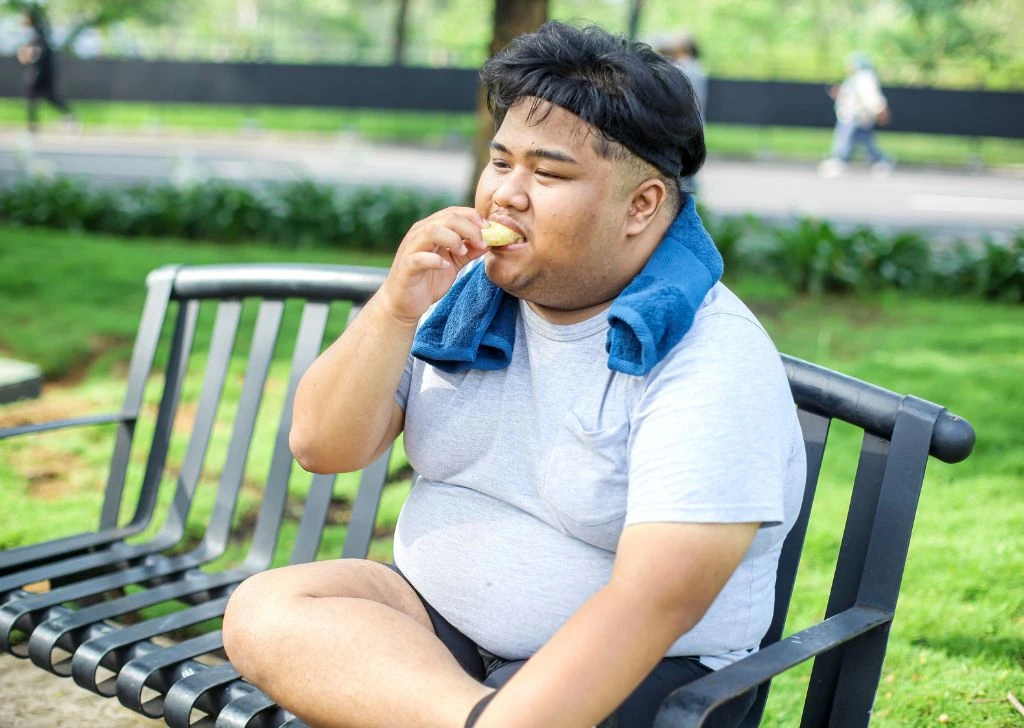 An overweight man snacking and neglecting his exercise. 
